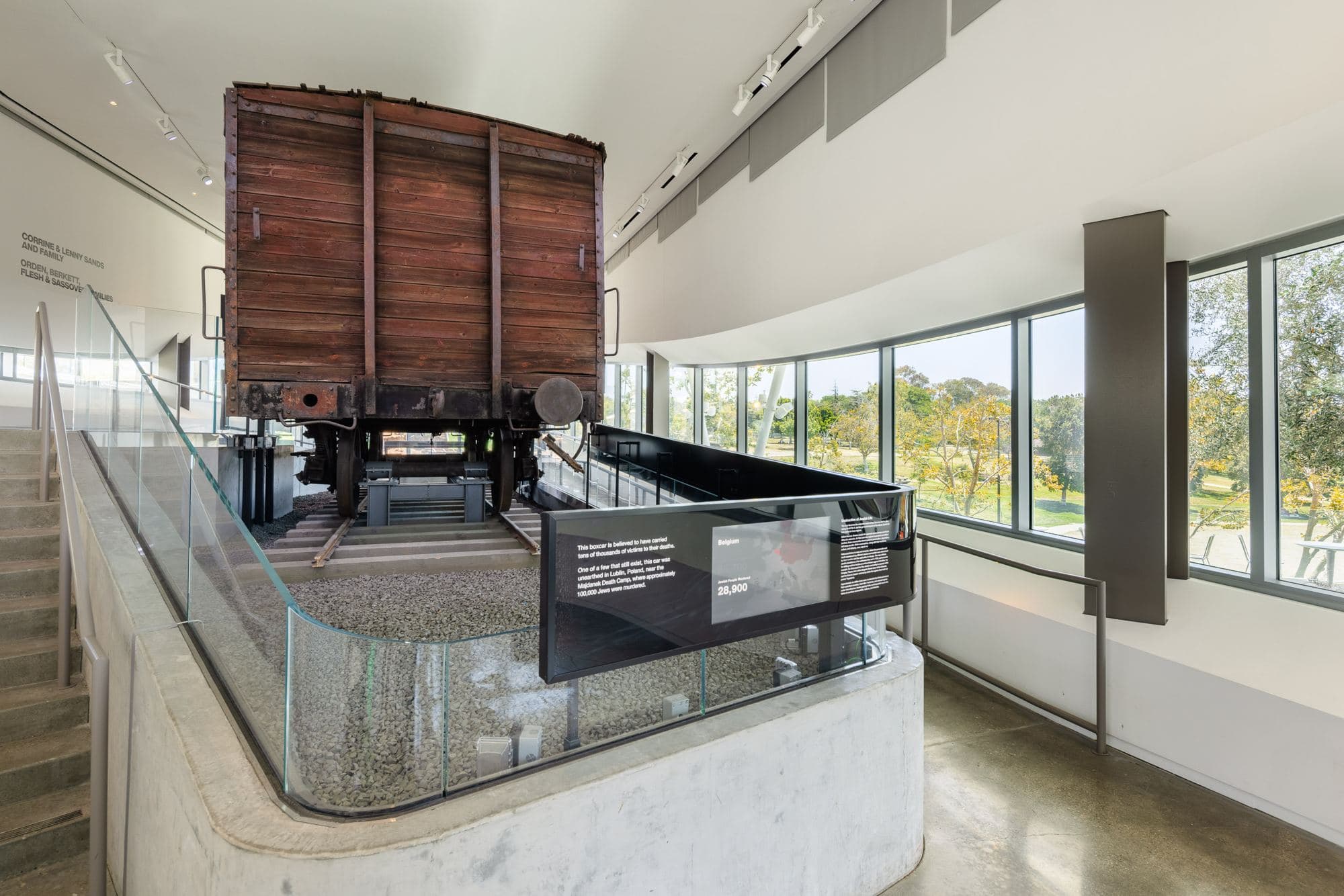 The Majdanek boxcar on its rails inside the glass-walled Boxcar Pavilion, with the park beyond