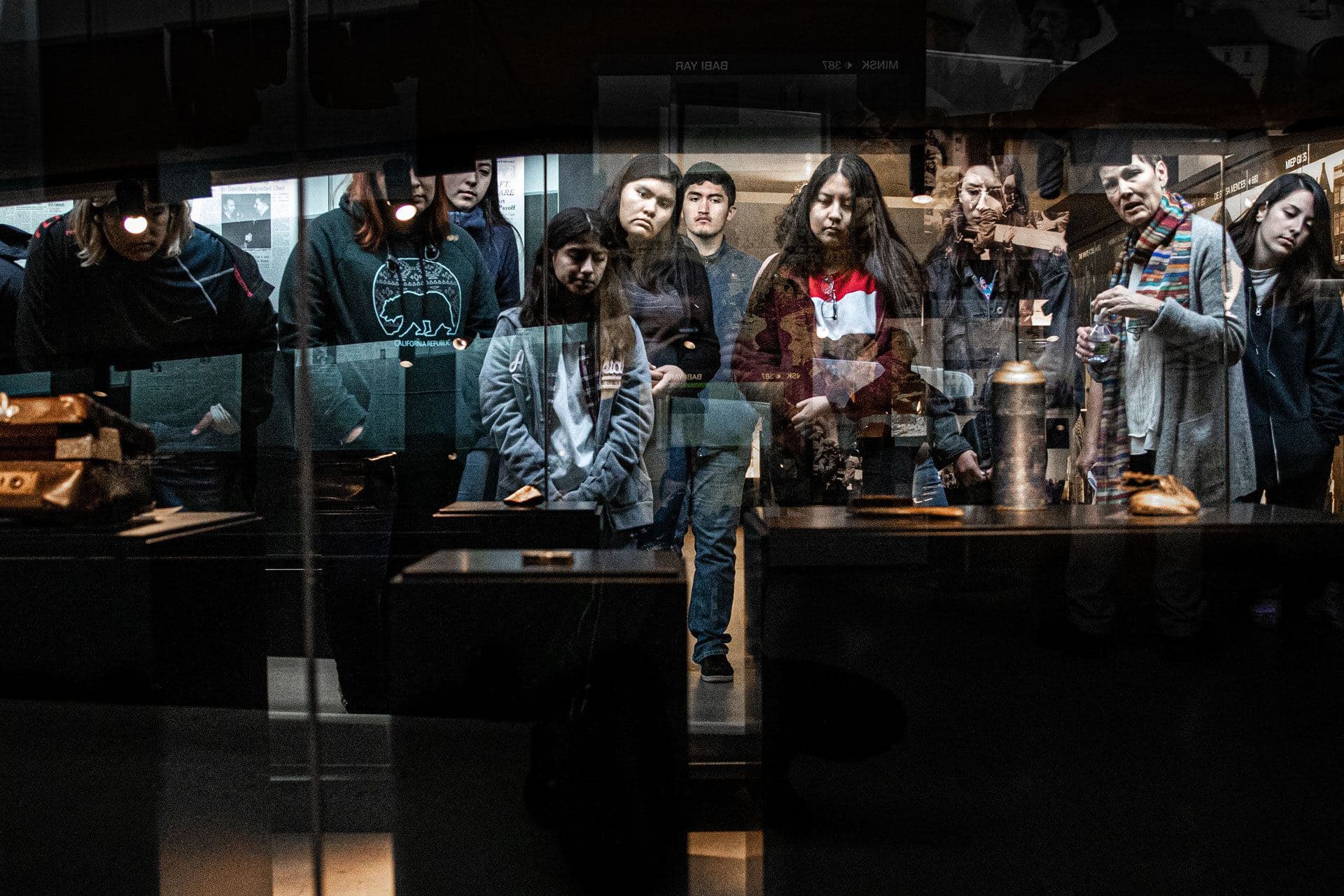 A docent leads students through an artifact case in the permanent exhibition, seen through the glass